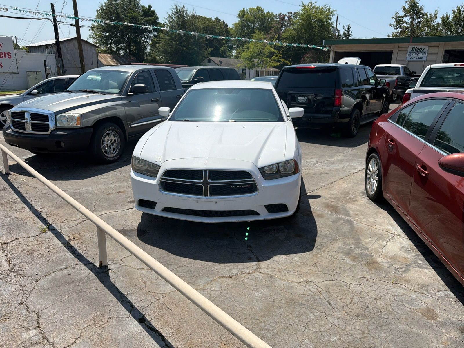 White Dodge Charger parked in a crowded outdoor lot beside black and red vehicles.