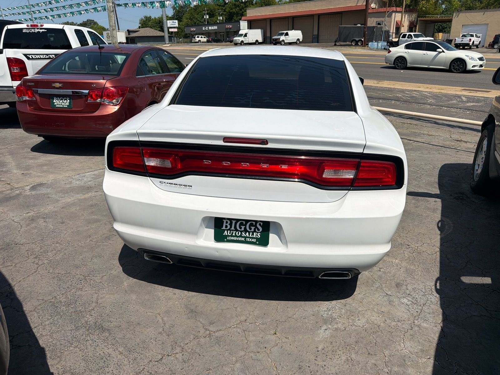 White Dodge Charger parked in a lot, rear view with a red taillight strip and green license plate.
