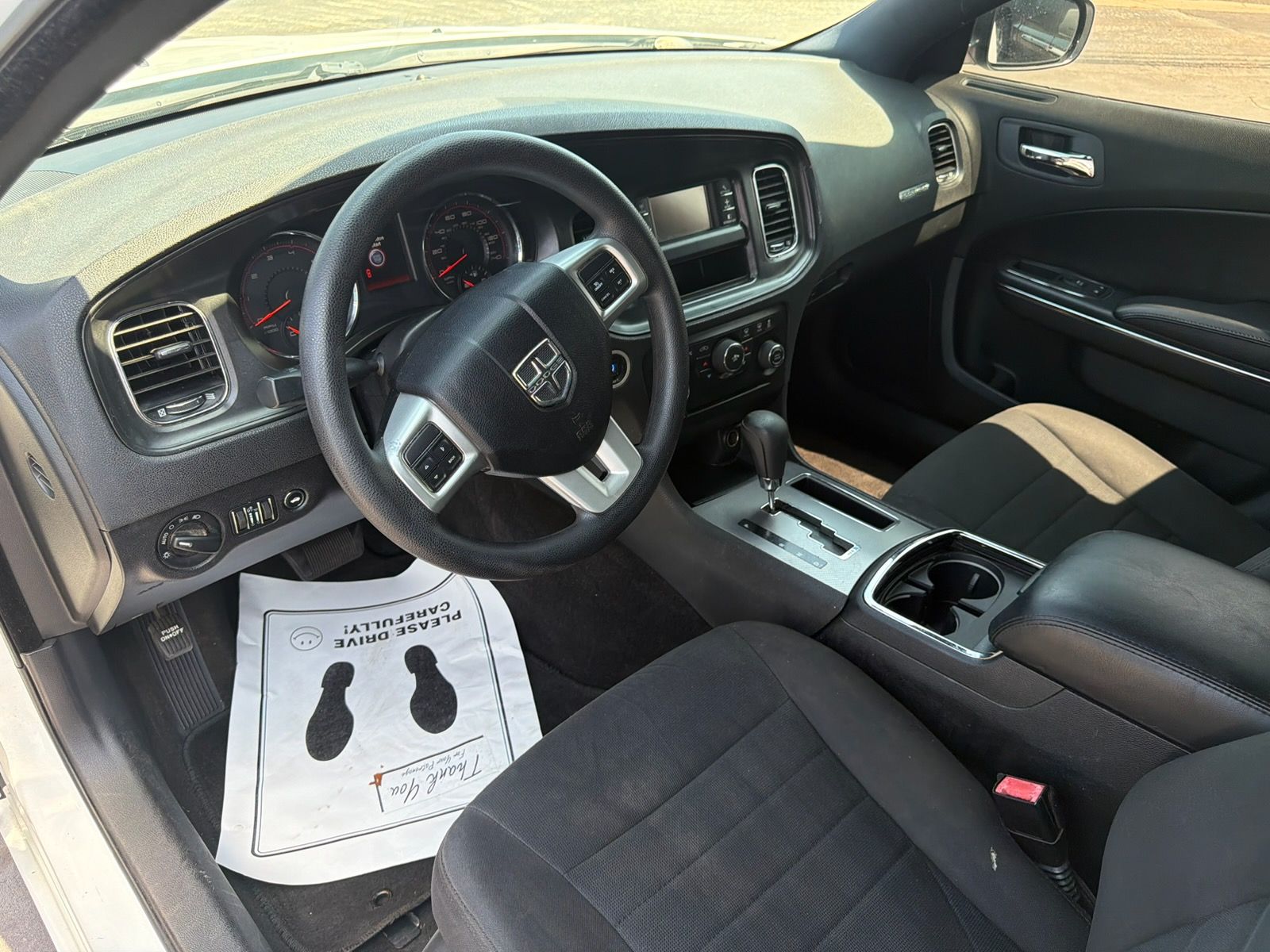 Car interior with black seats, steering wheel, center console, and a paper floor mat on the driver’s side.