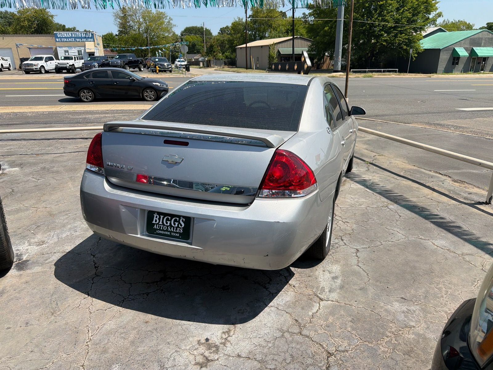 Silver sedan parked by a roadside, rear view, with street and traffic in the background