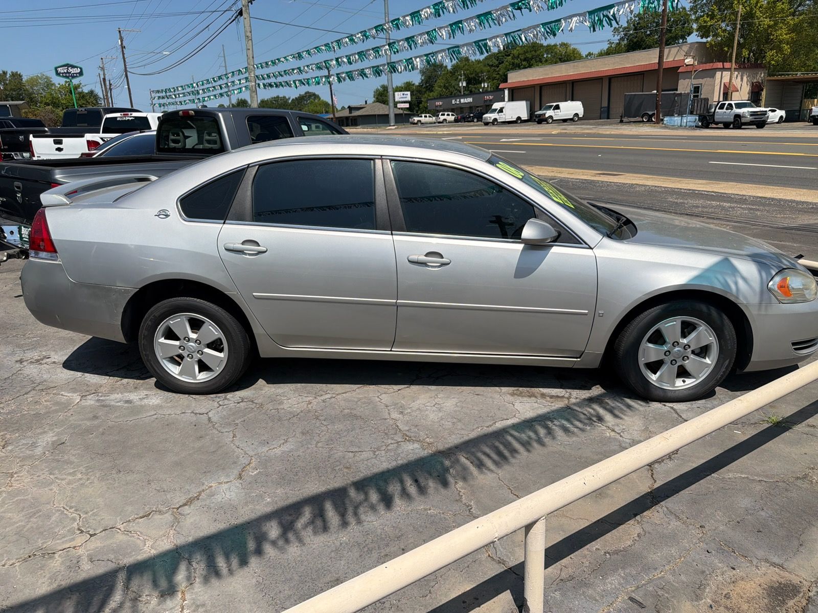Silver sedan parked beside a curb in a sunny parking lot under string lights.