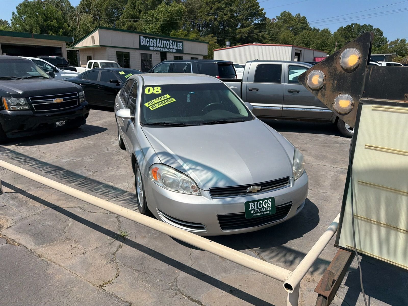 Silver sedan with neon sale stickers parked at a car lot, viewed from the front.