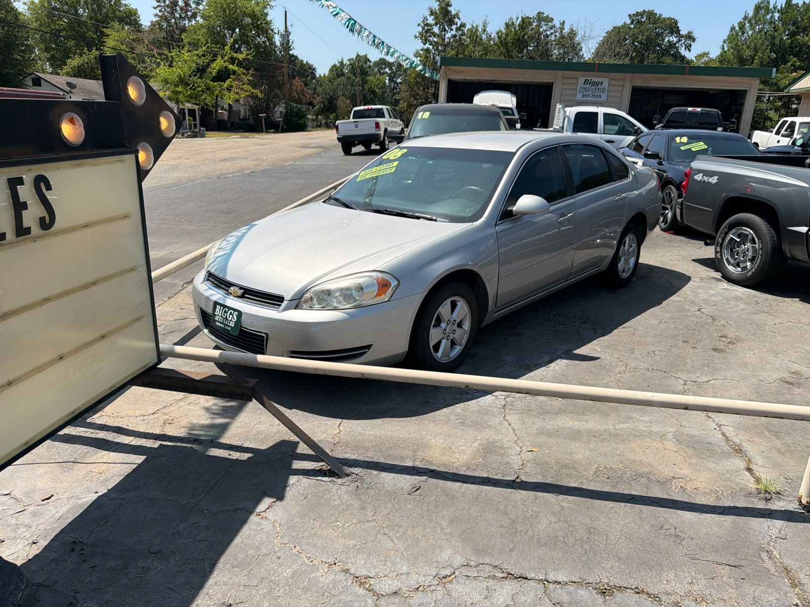 Silver sedan parked in a sunlit lot beside a black pickup and a sign