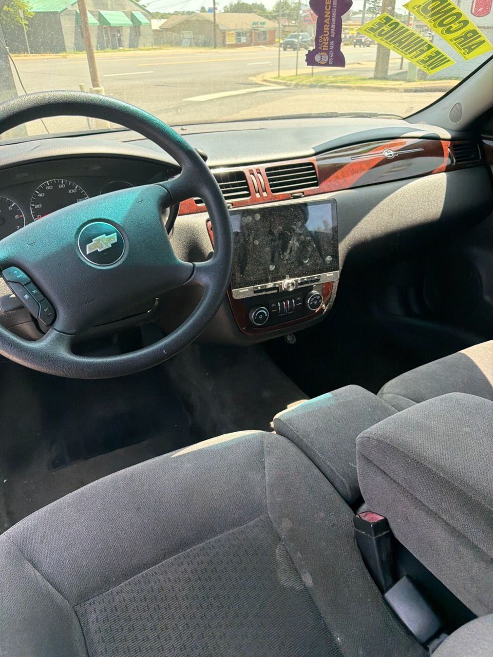 Car interior with steering wheel, dashboard screen, and front passenger seat in daylight.