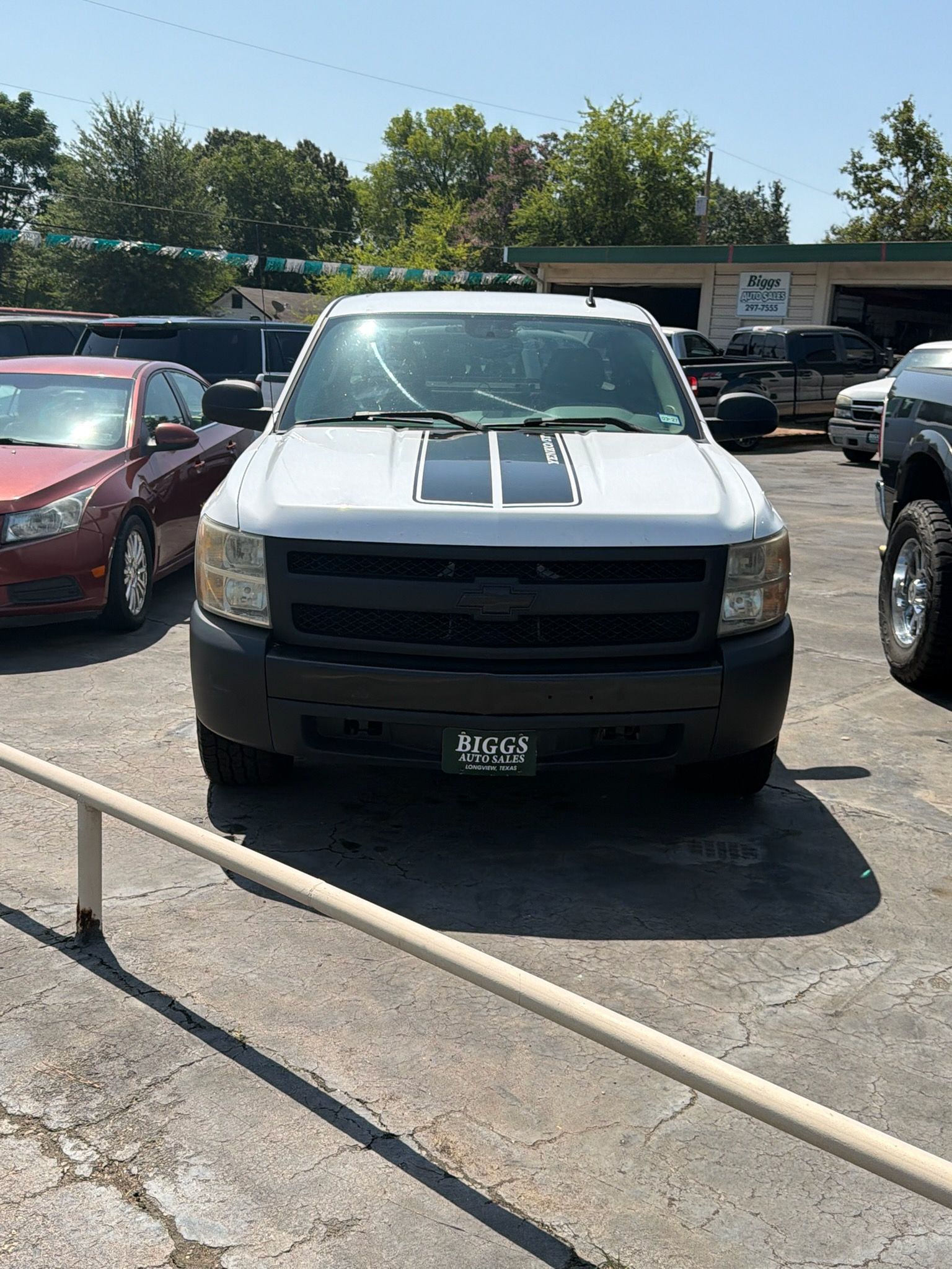 White pickup truck parked in a lot, facing forward, with other vehicles around it.