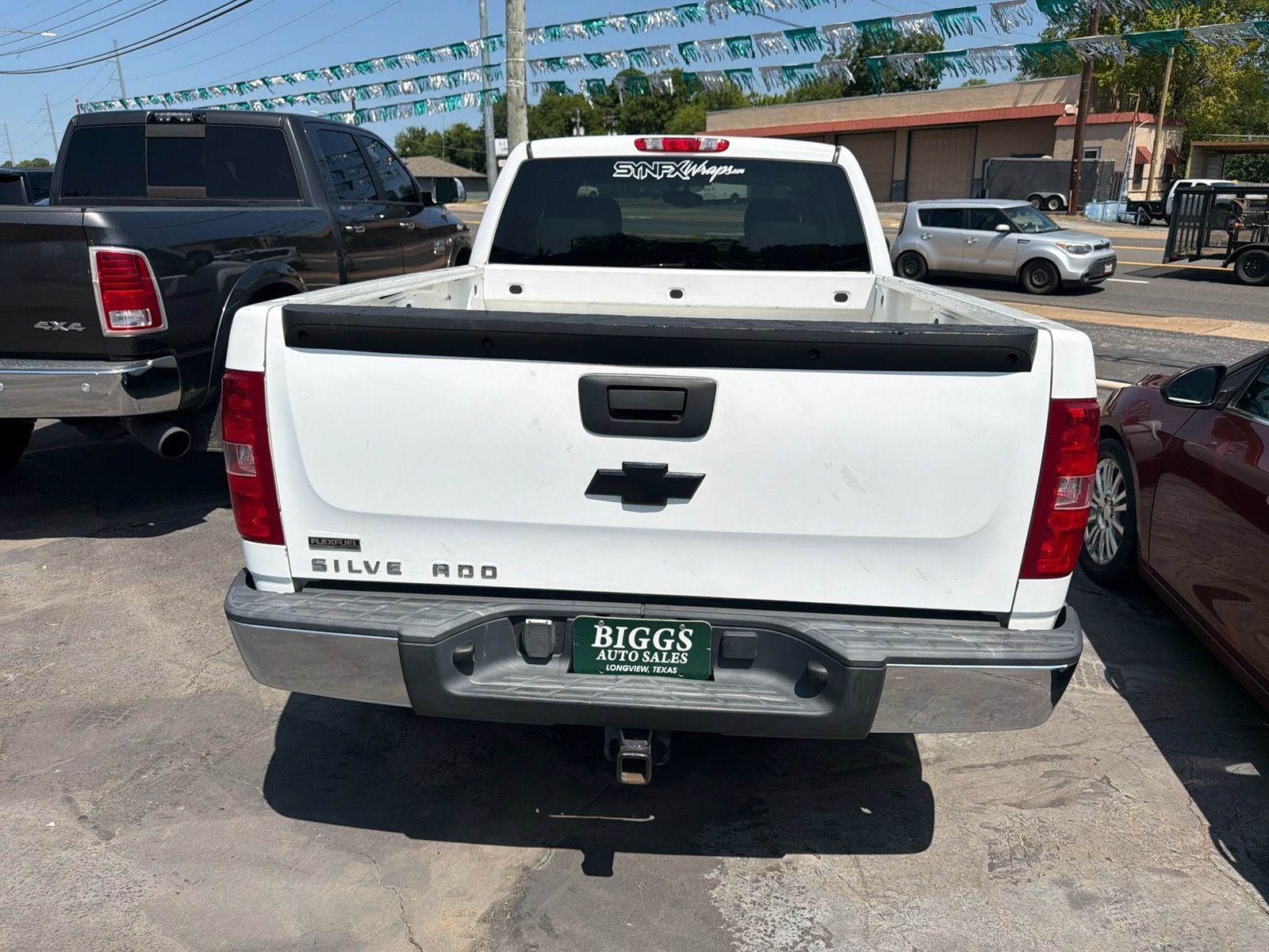 White Chevrolet Silverado pickup parked between a black truck and a red car in a parking lot.