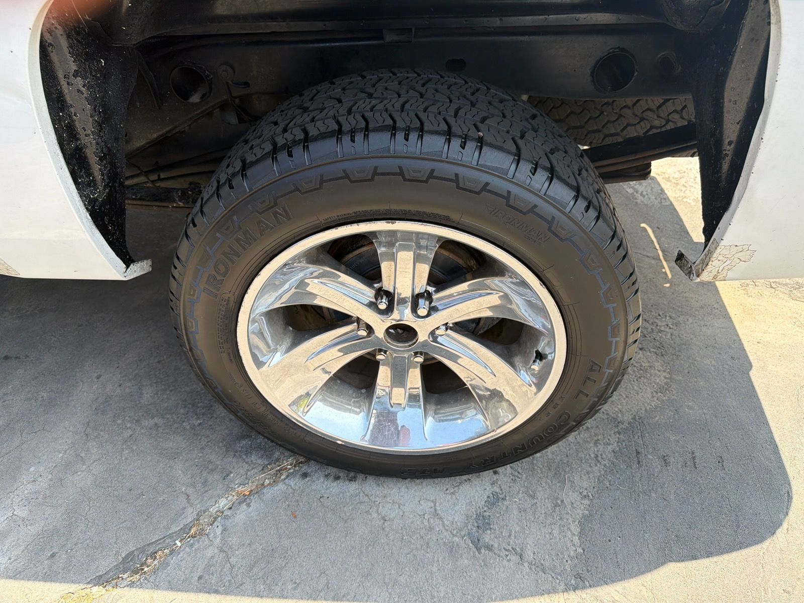 Flat tire on a black truck parked on pavement, showing a chrome wheel and side panel.