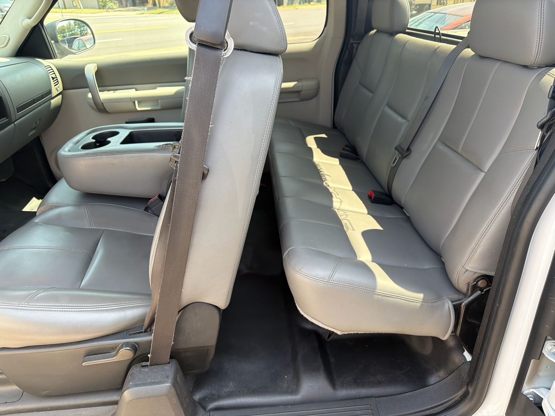 Tan leather car back seat with a fold-down center armrest and sunlight streaming in.