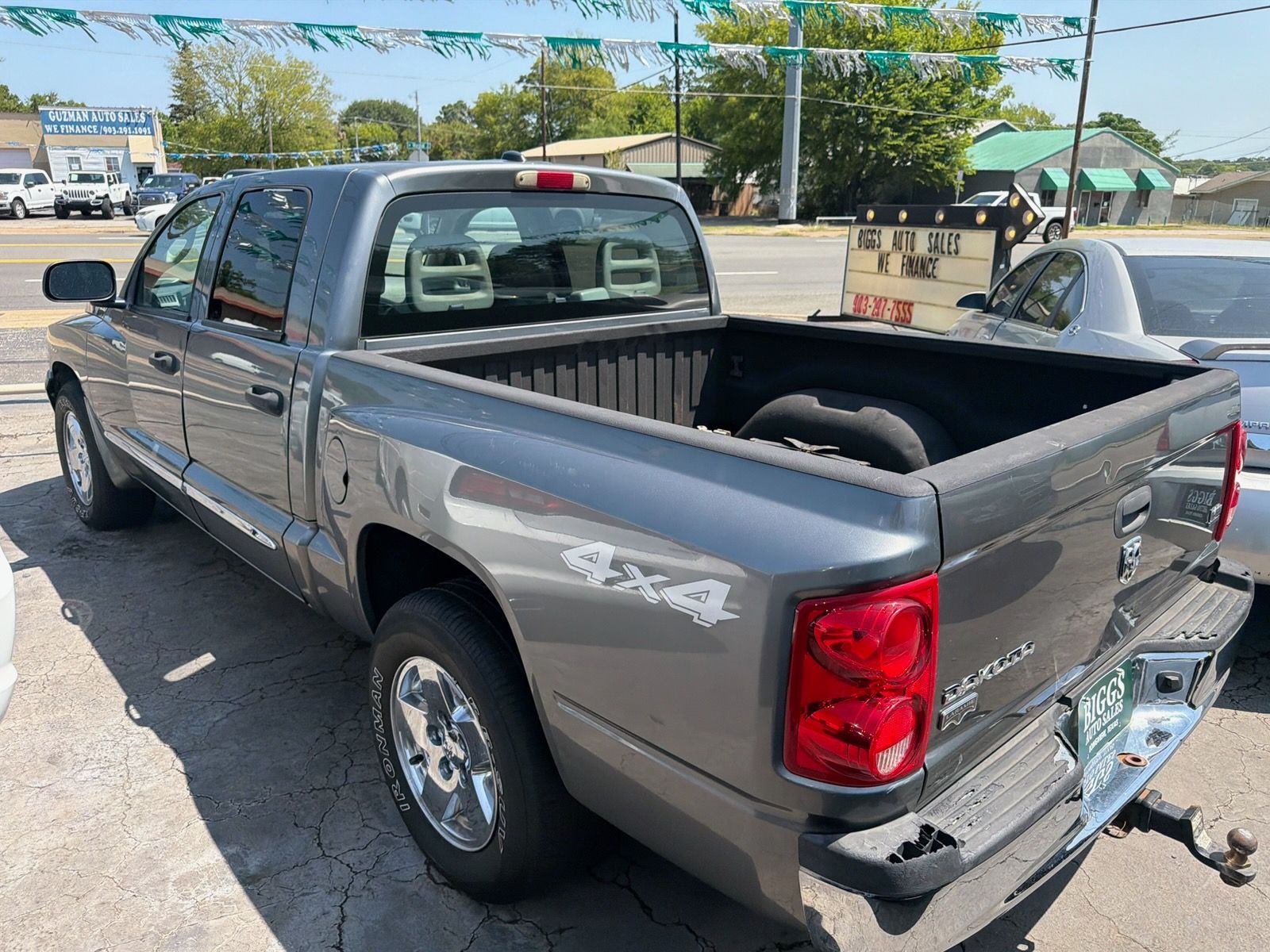 Gray pickup truck parked in a lot, rear side view, with an open bed and tow hitch