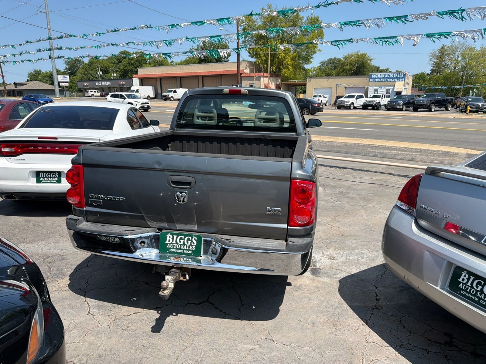 Rear view of a damaged black pickup truck in a parking lot, with a bent bumper and tow hitch visible.