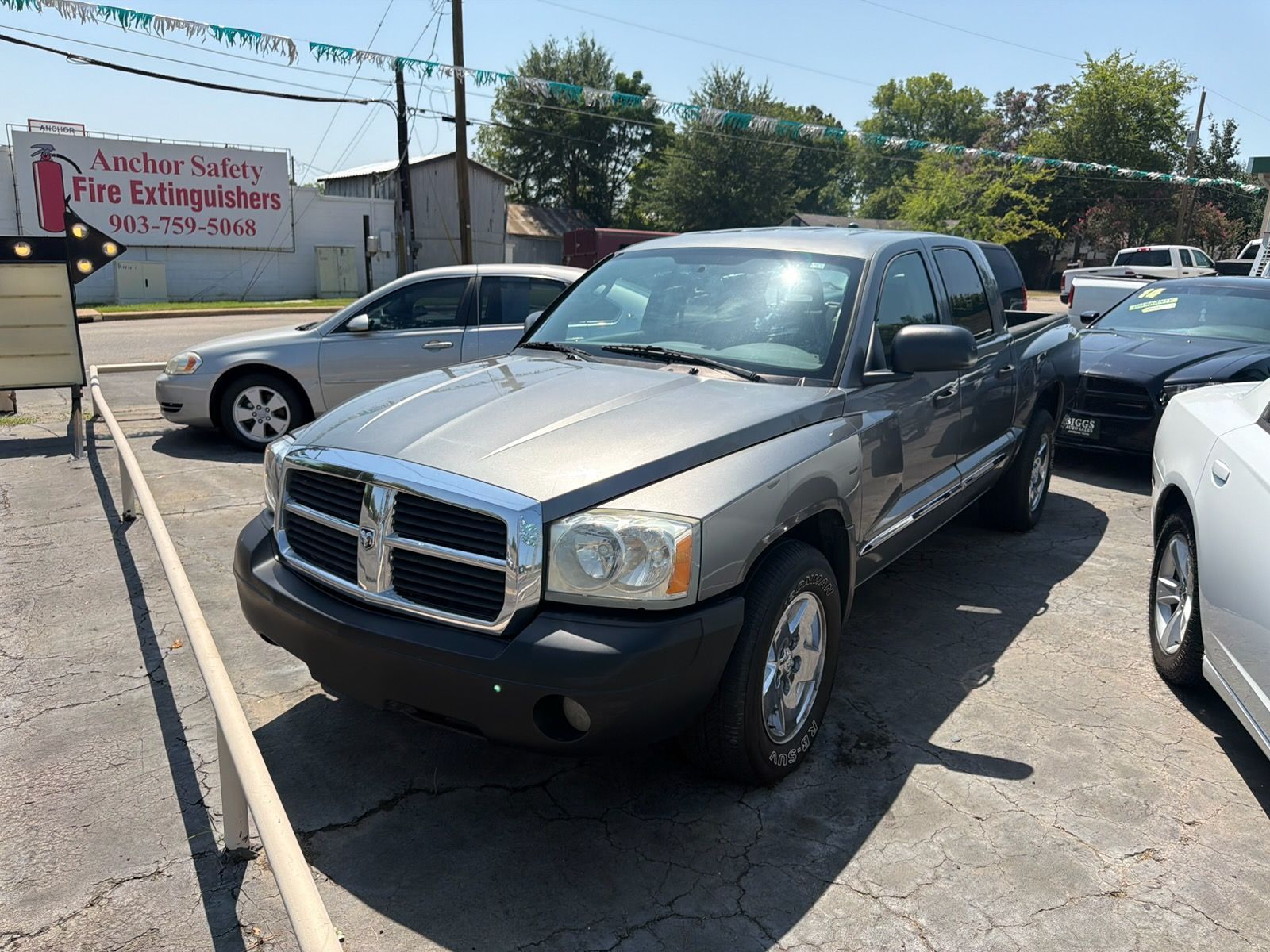 Gray pickup truck parked at a car lot, front view with other cars nearby.