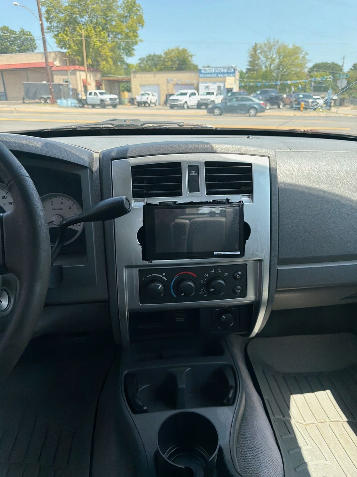 Car dashboard and center console with aftermarket touchscreen, parked outdoors in daylight.