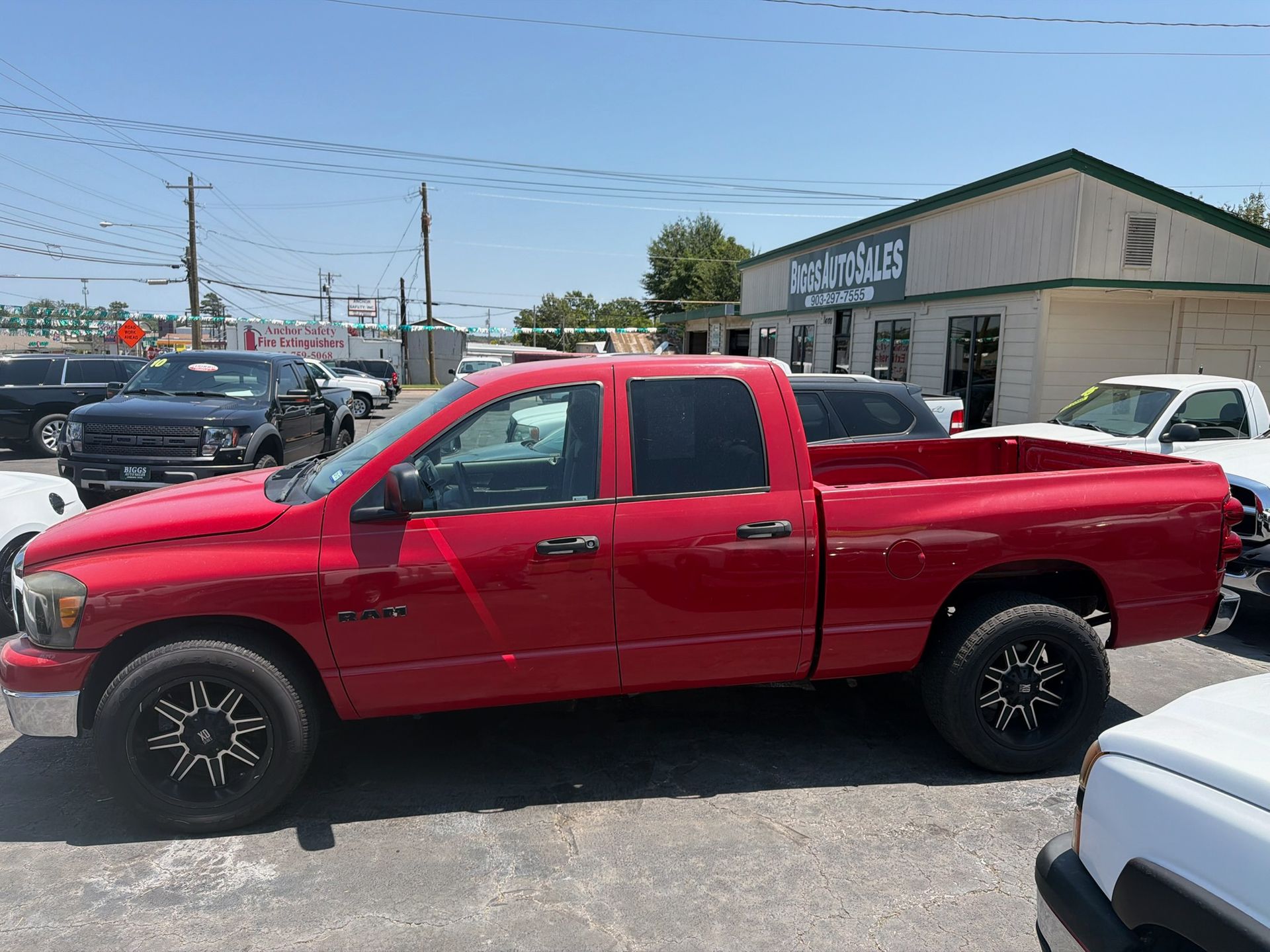 Red lifted pickup truck parked in a lot beside a building under a bright blue sky