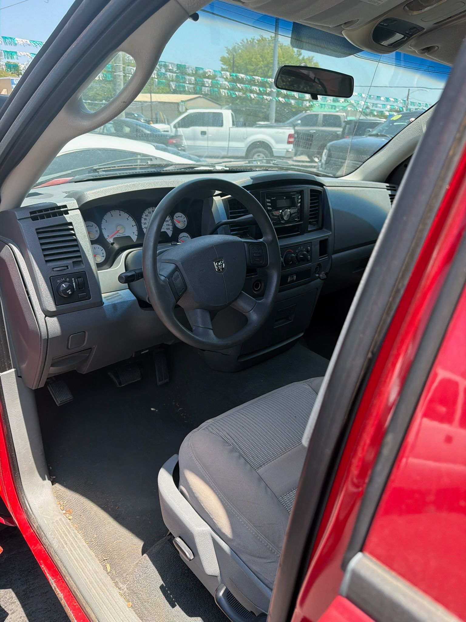 Open car door showing gray interior, black dashboard, steering wheel, and front seat in a red vehicle.