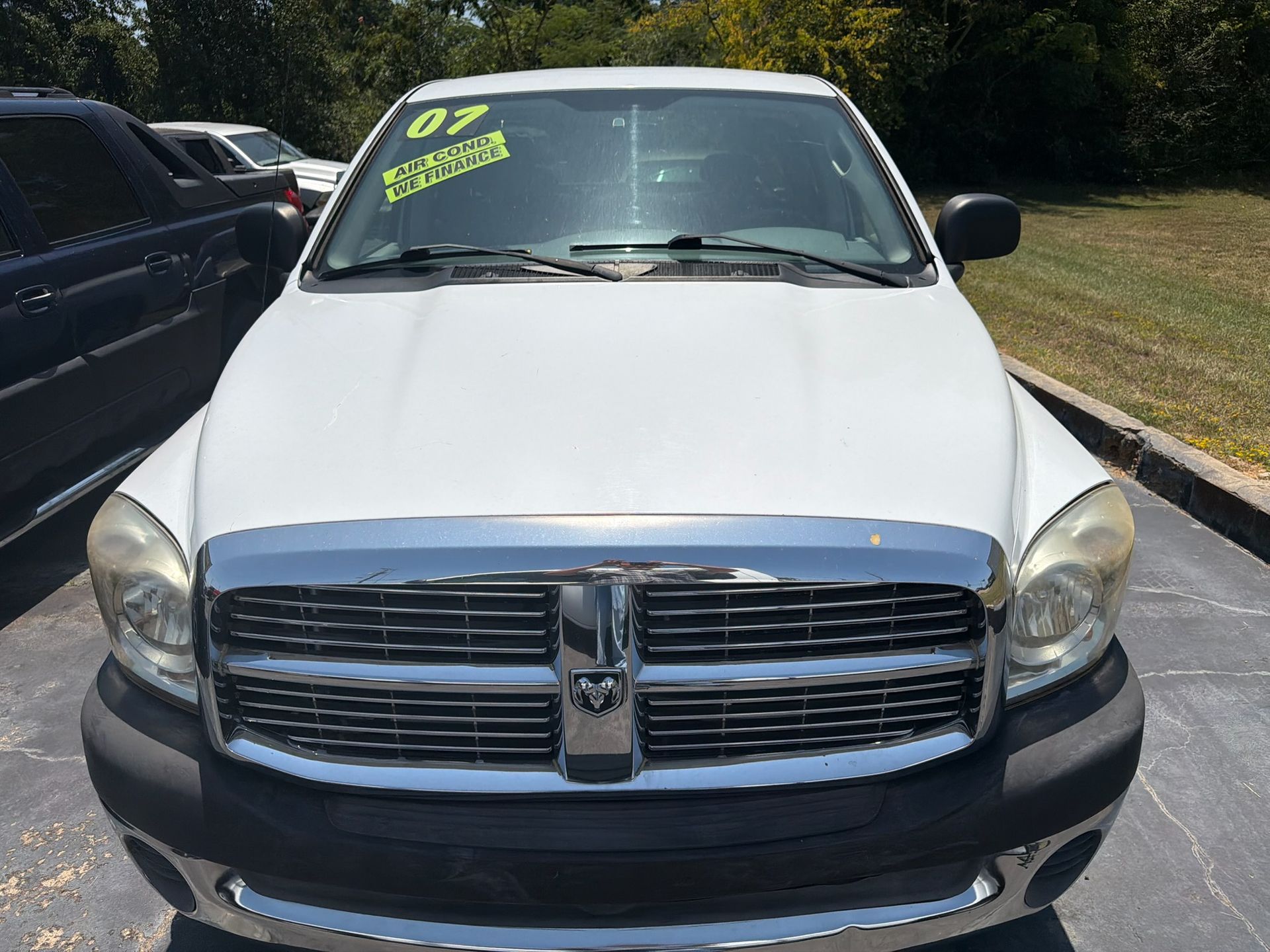 White Dodge Ram truck parked outdoors with a neon sale sticker on the windshield