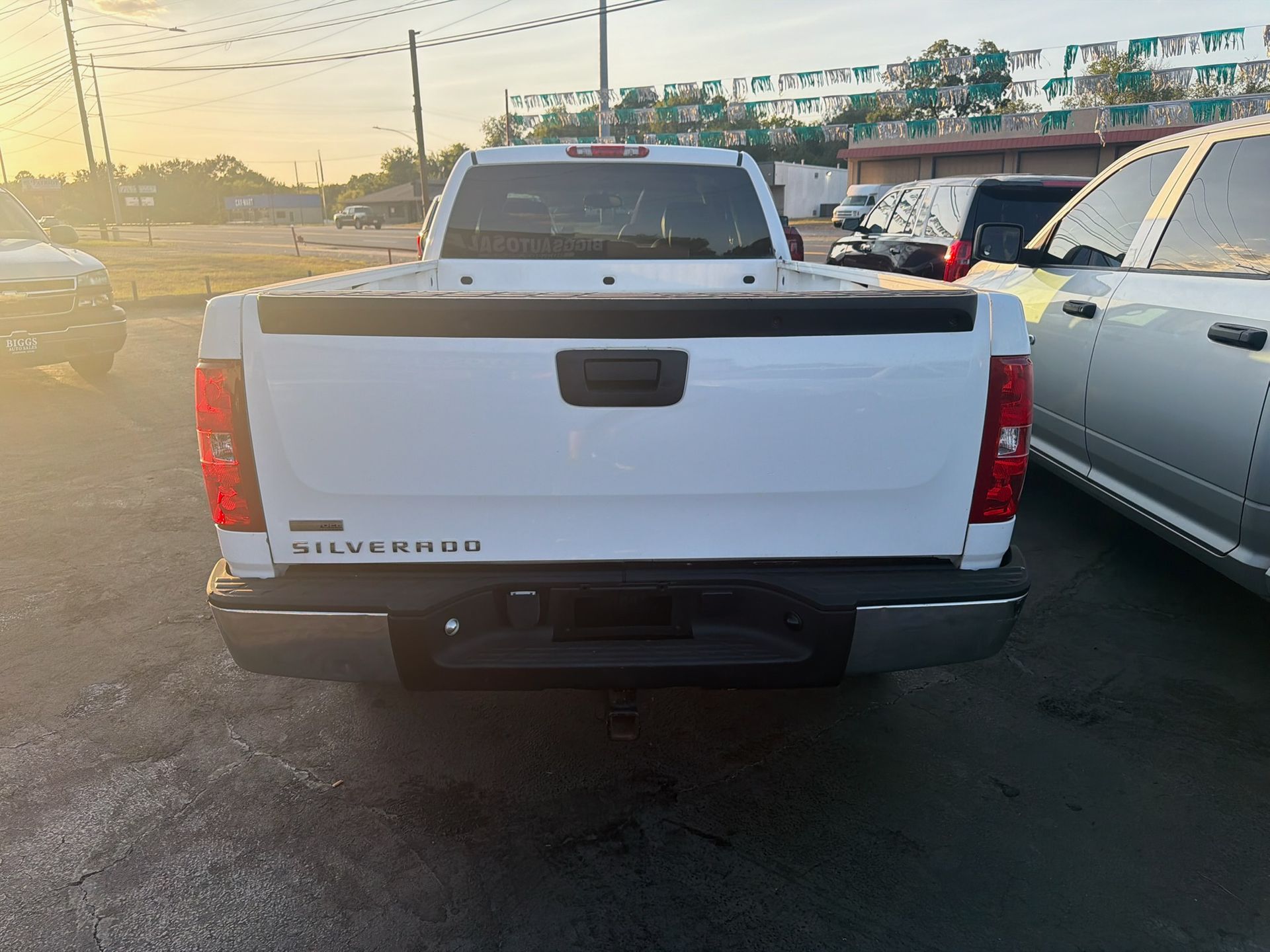 White GMC pickup truck seen from the rear in a parking lot at sunset
