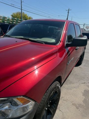Red pickup truck parked outdoors in bright sunlight, showing front-left side and black wheels.