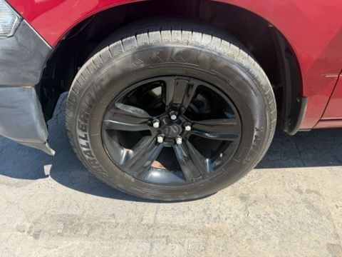 Close-up of a red car’s front wheel with a black alloy rim on pavement.