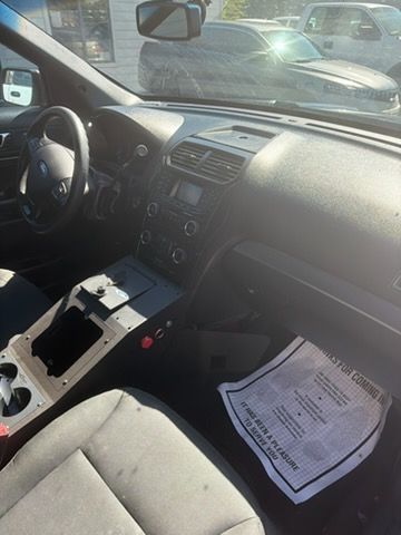 Car interior with center console removed, papers on passenger seat, parked in bright sunlight