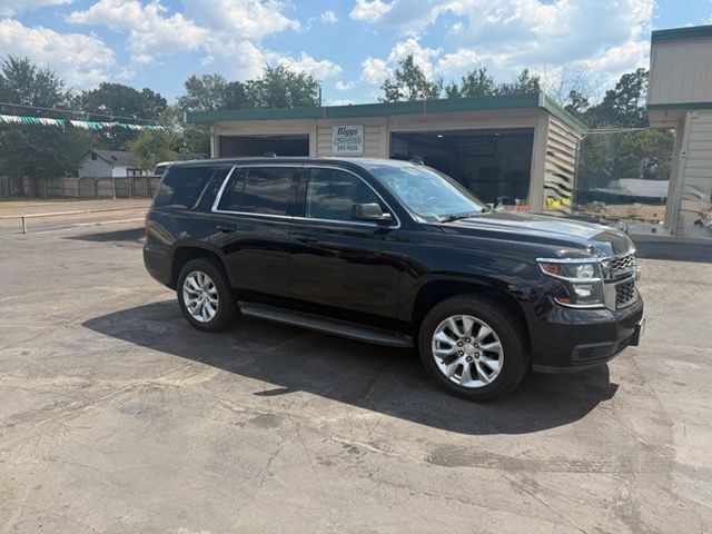 Black SUV parked on a sunlit lot near low buildings and trees.