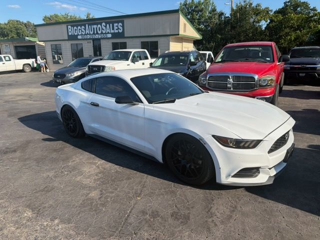White sports coupe parked in a car lot with dealership buildings and other vehicles in the background