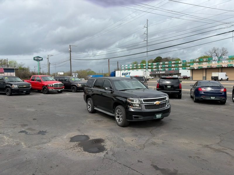 Parking lot with several cars under a cloudy sky, centered on a black SUV and red car on the left.