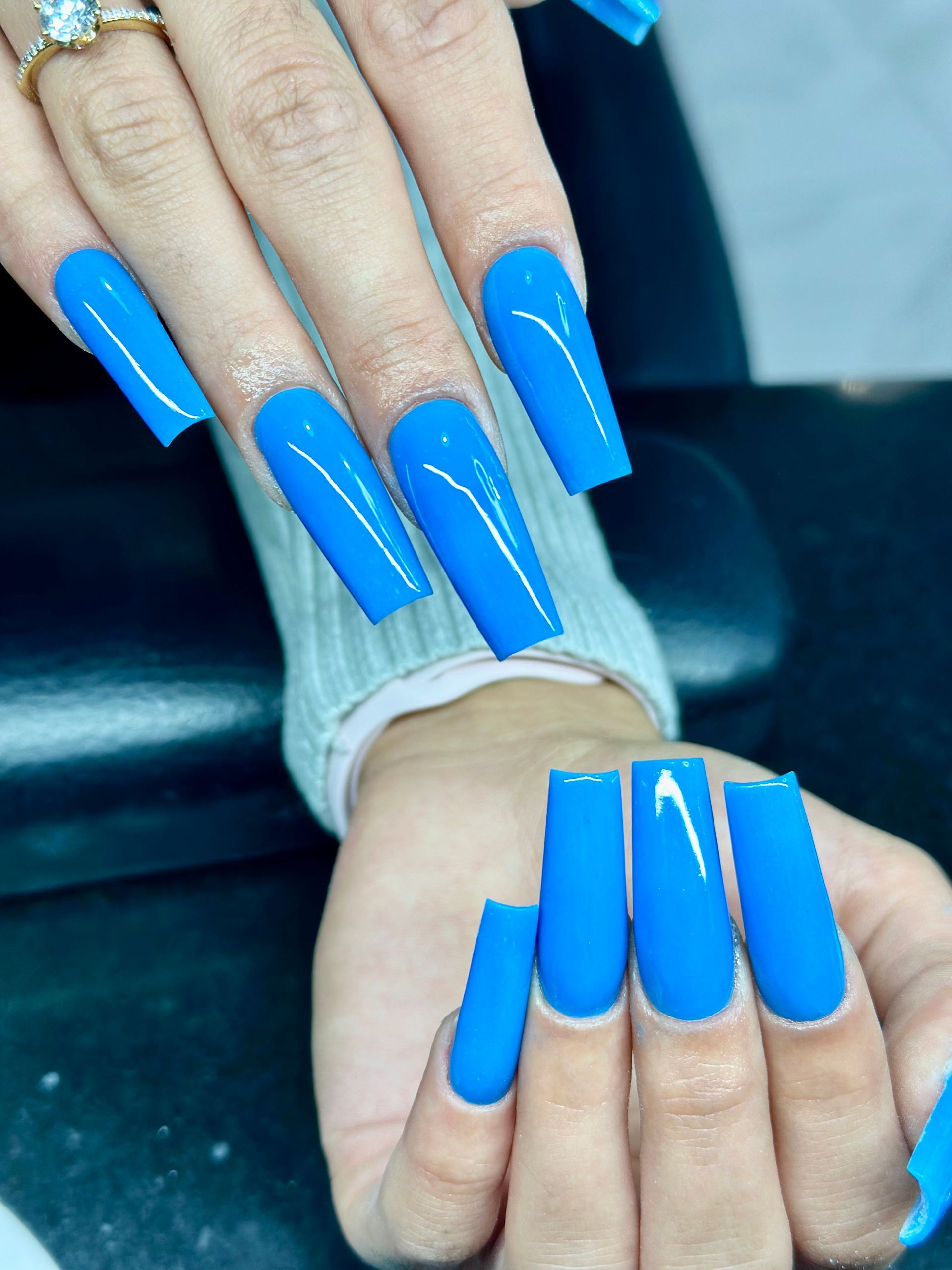 Die Hand einer Frau mit langen blauen Nägeln und einem Ring am Finger.