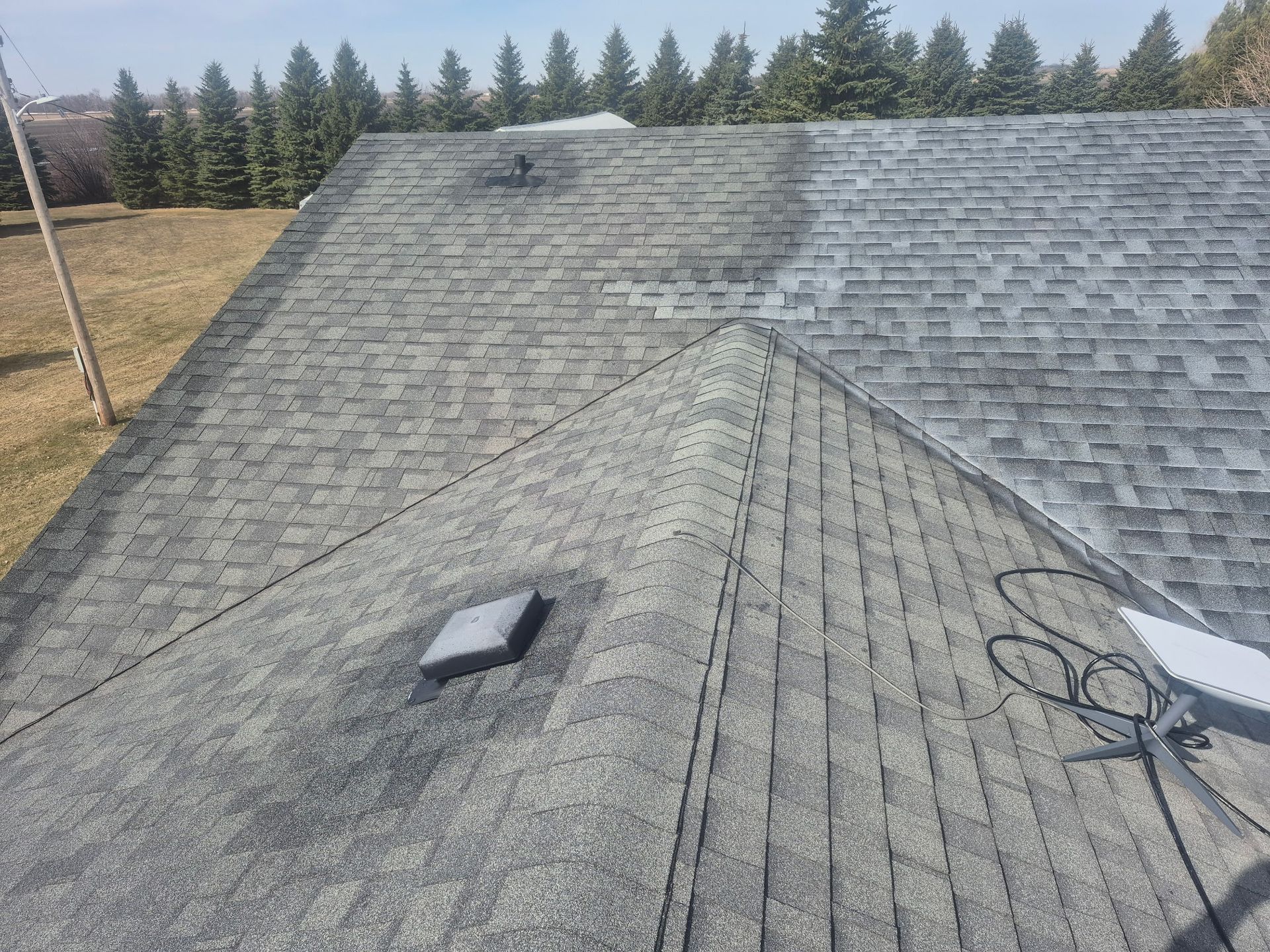 Gray shingled roof with a central ridge, small skylights, and trees in the background