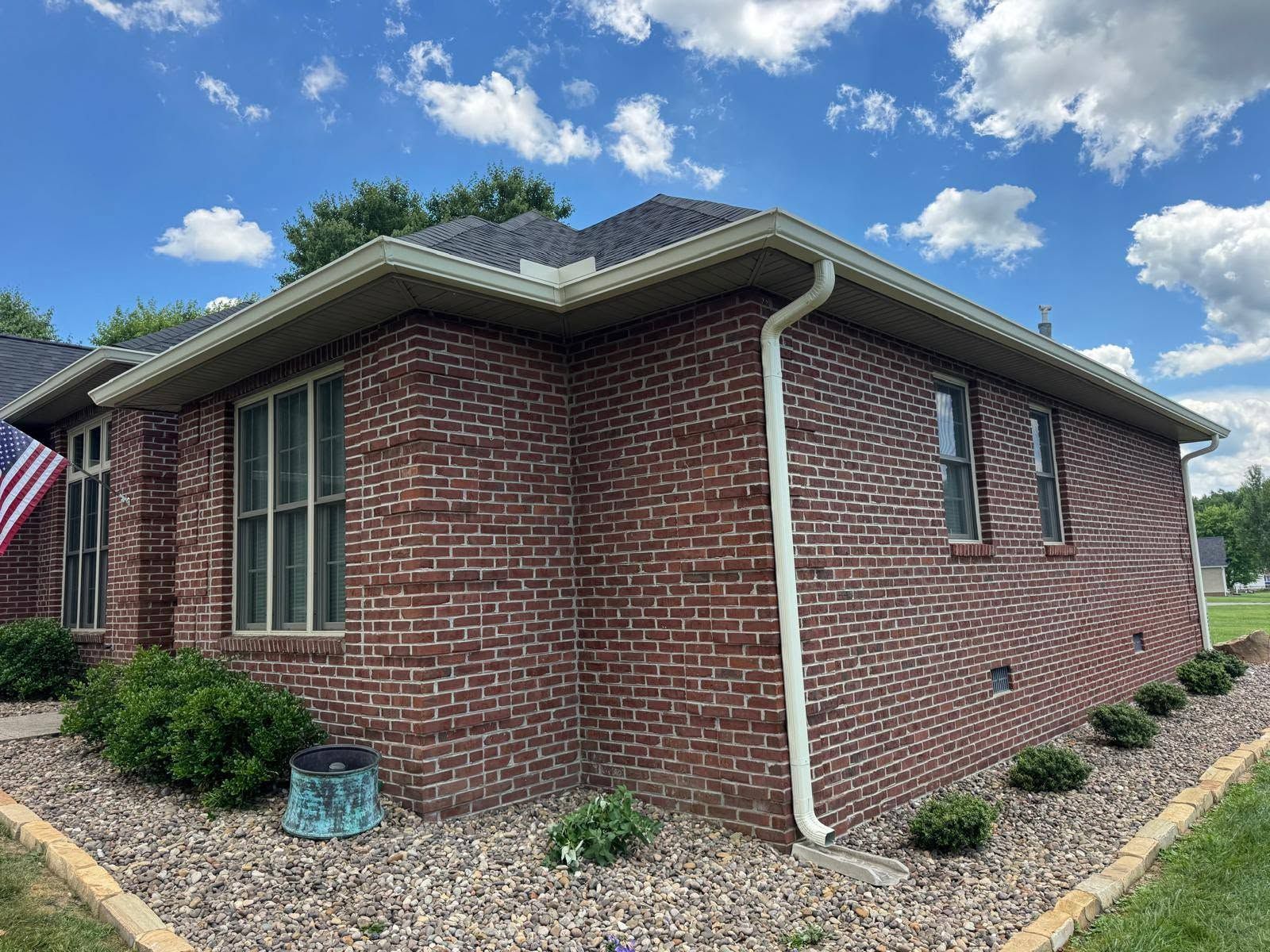 Single-story red brick house with white trim and landscaped gravel yard under a cloudy sky