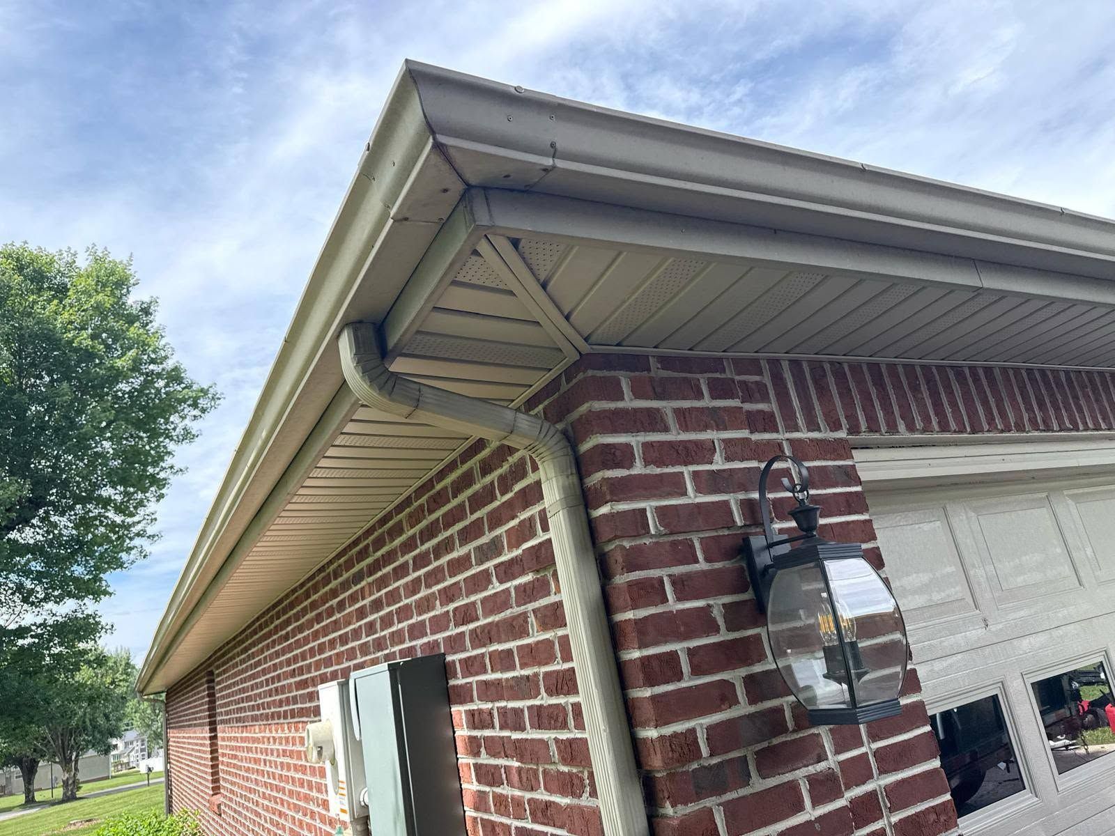Brick house corner with white garage door, porch light, and beige gutters under a clear sky