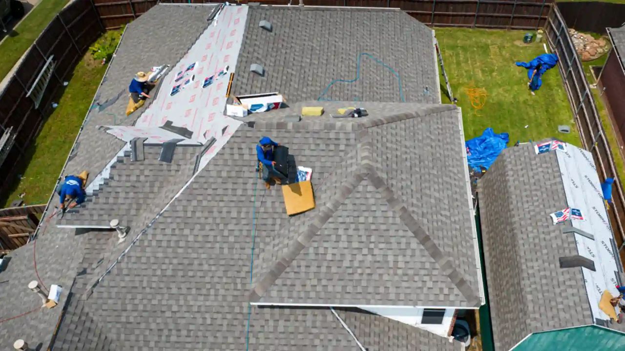Roof under repair with workers, blue tarps, and roofing materials on a house