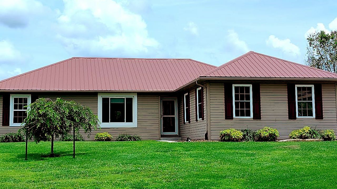 Single-story beige house with red roof and green lawn under a blue sky