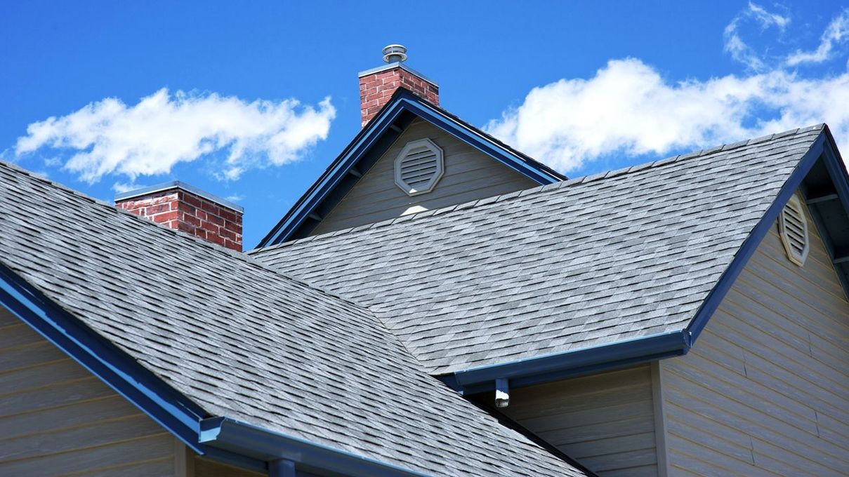 Blue-gray shingled house roofs against a bright blue sky with clouds