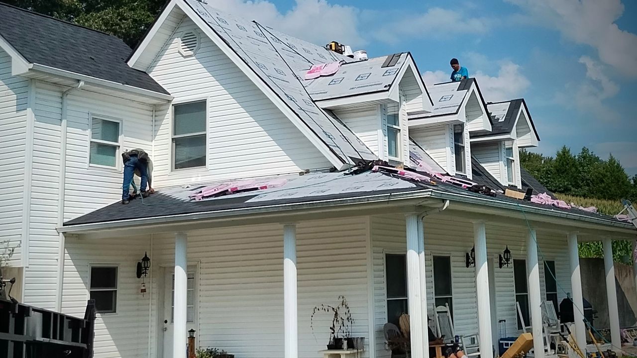 White house with damaged roof and workers repairing it from the top, with a porch in front