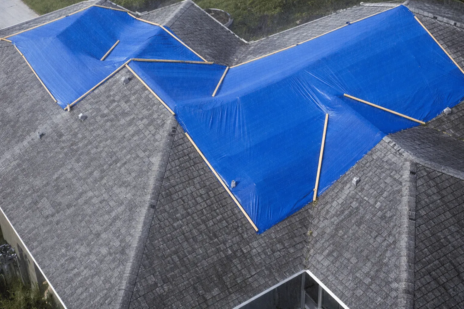 Blue tarp-covered roof damage on a gray shingled house