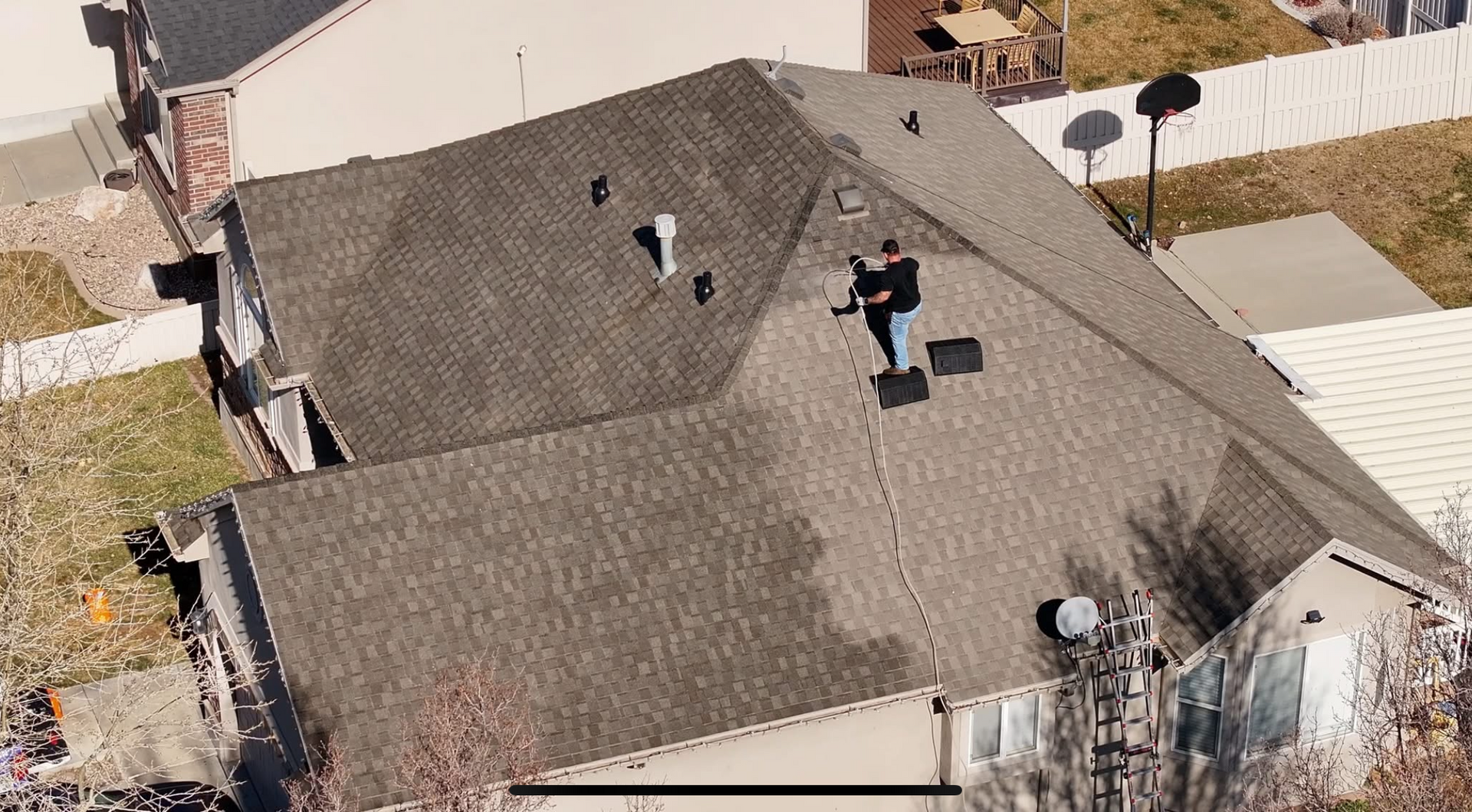 Aerial view of a house roof with shingles, vents, and chimneys in a residential neighborhood.
