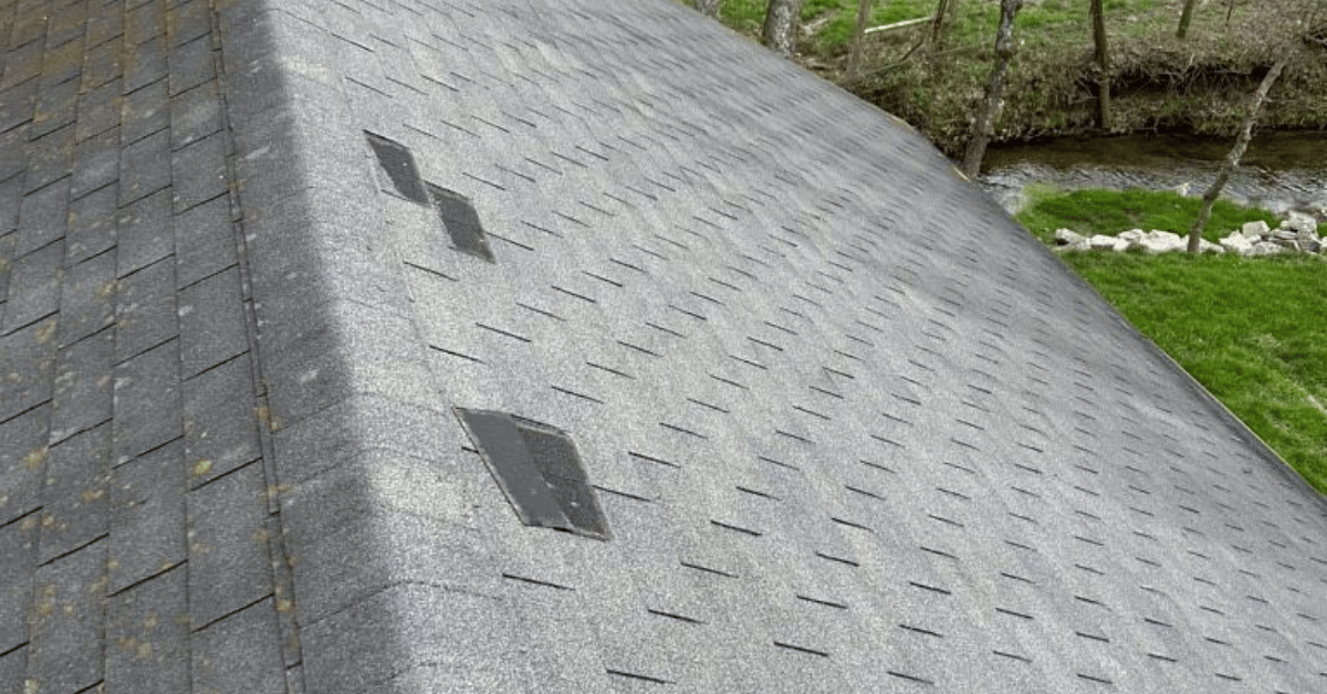 Slate roof with a small skylight and grass border beside a stone wall