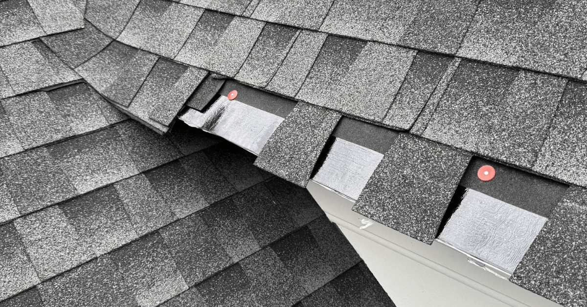 Damaged gray shingle roof with several shingles lifted, exposing underlayment and fasteners