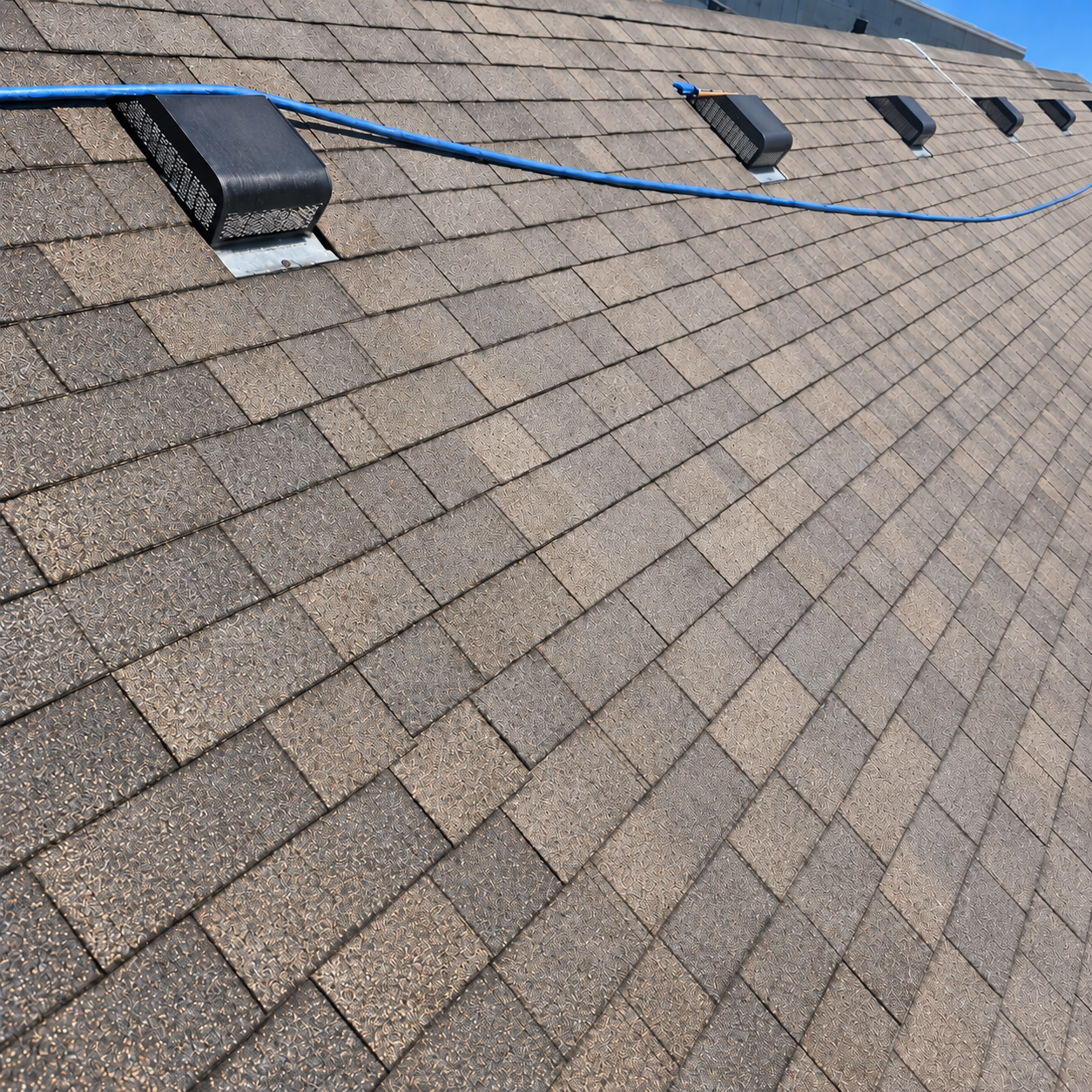 Close-up of a dark gray asphalt shingle roof with a light gray gutter at the edge