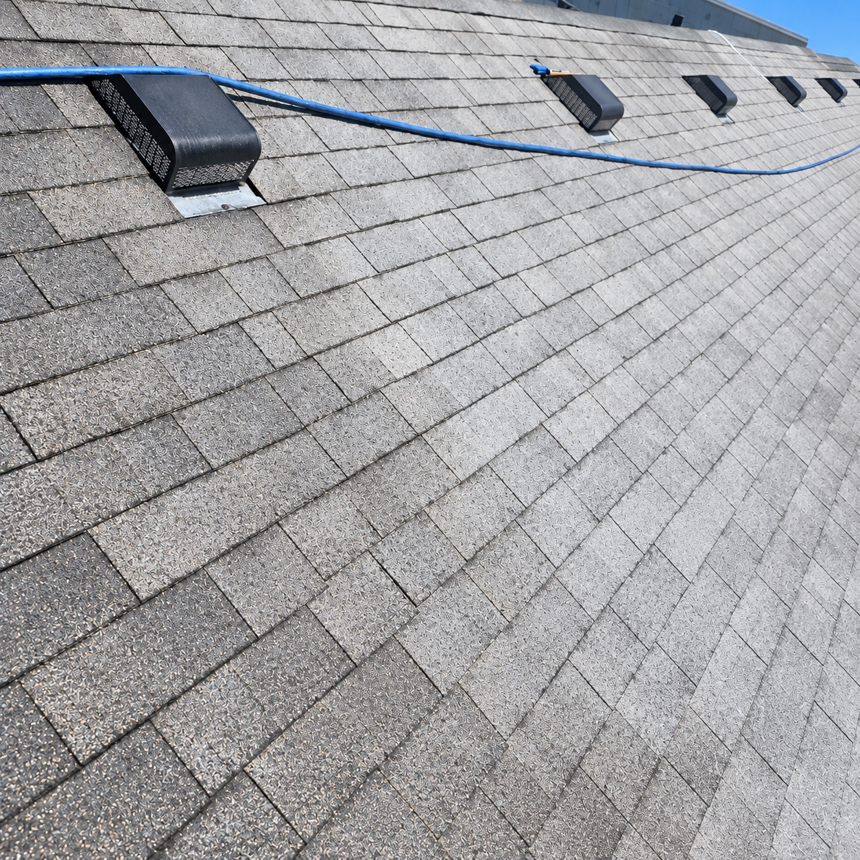 Cracked dark gray roof shingles with a damaged area in the center
