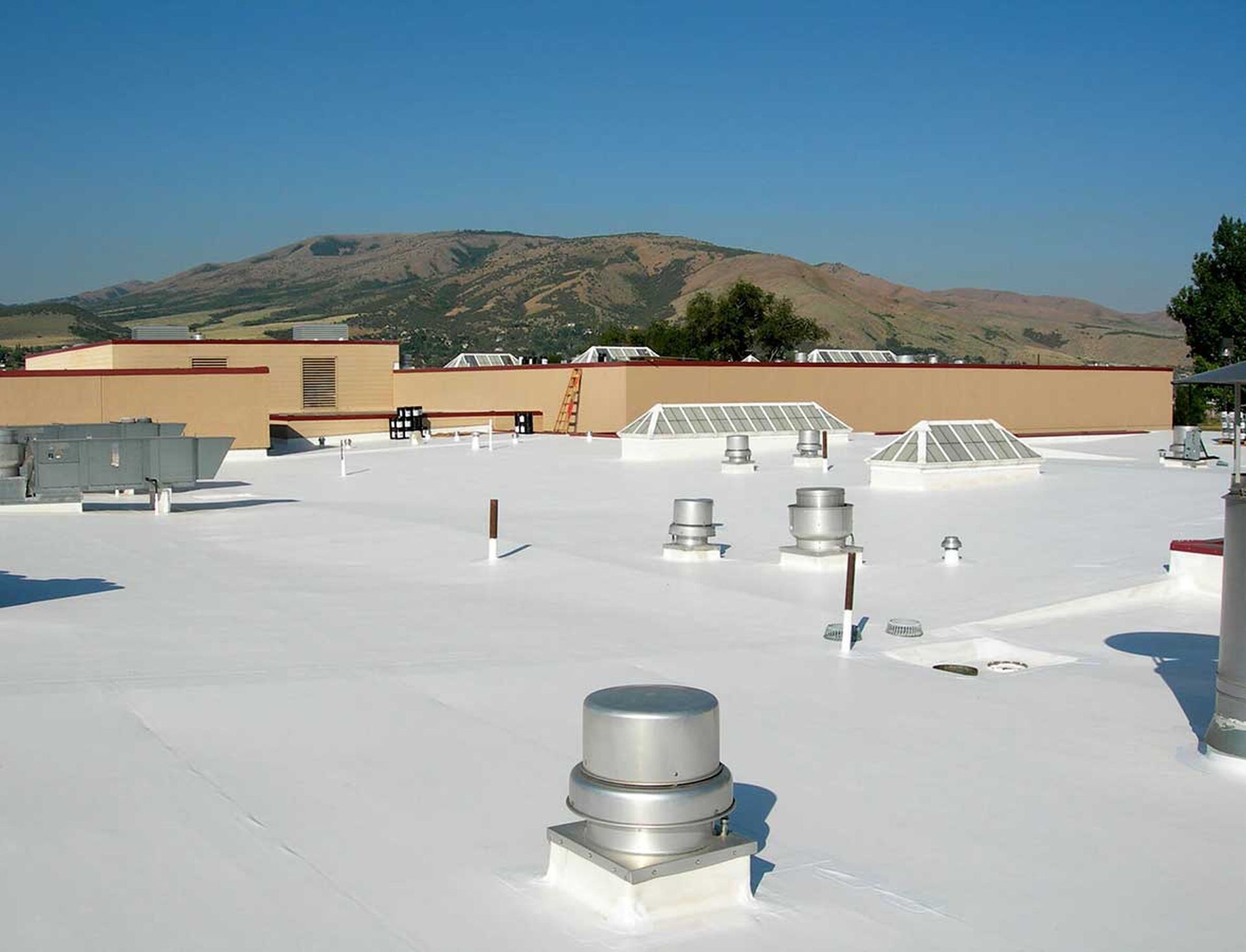 White flat rooftop with vents and distant mountain under a clear blue sky