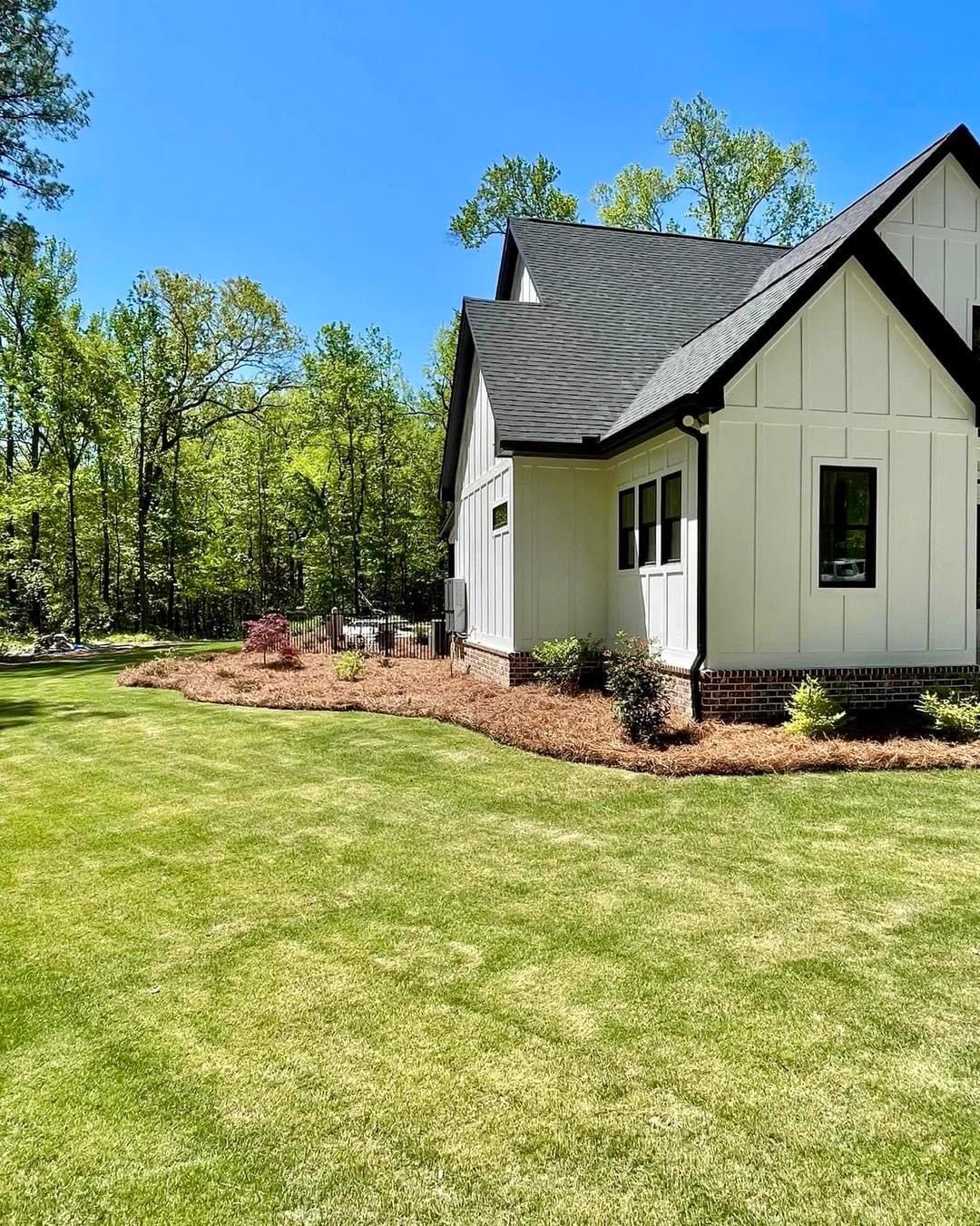 A white house with a black roof and a large lawn in front of it.