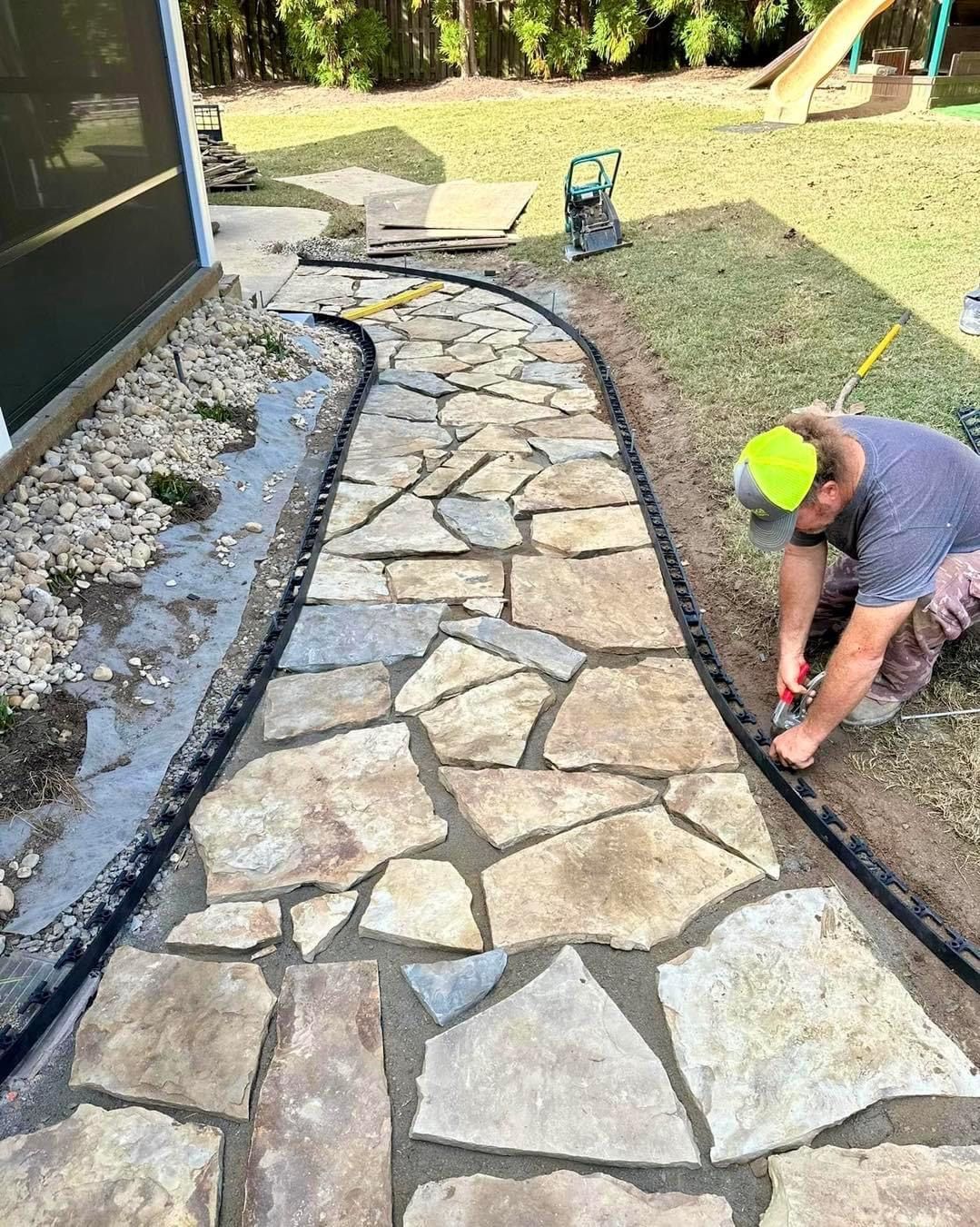 A man is working on a stone walkway in a backyard.