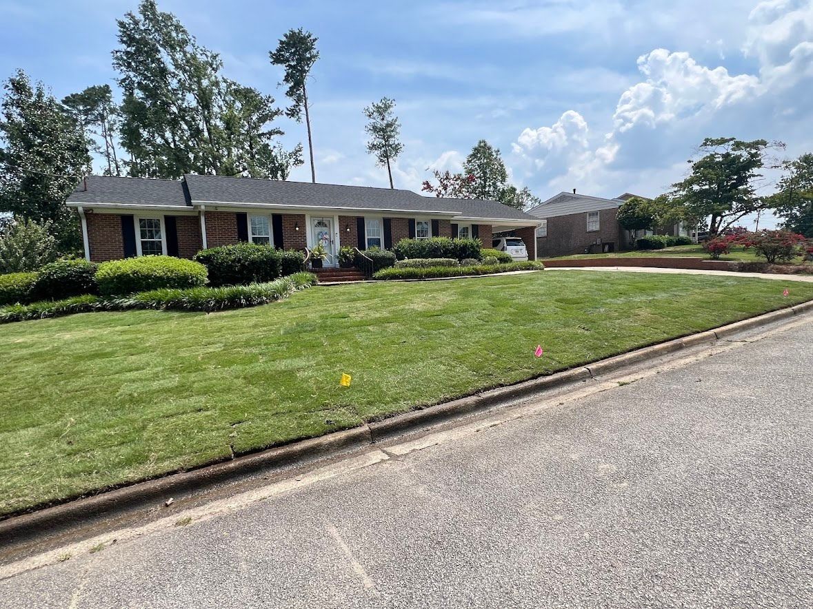 A brick ranch-style house with a well-kept lawn and landscaping on a sunny day.