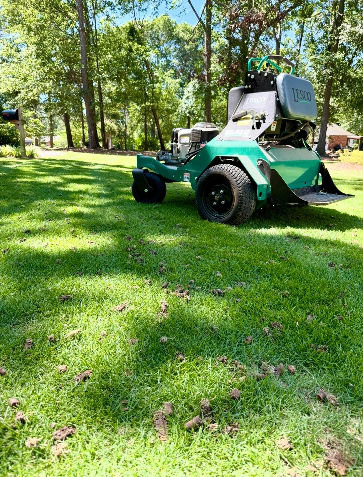 A green lawn aerator on a sunny day, in a yard with trees in the background.