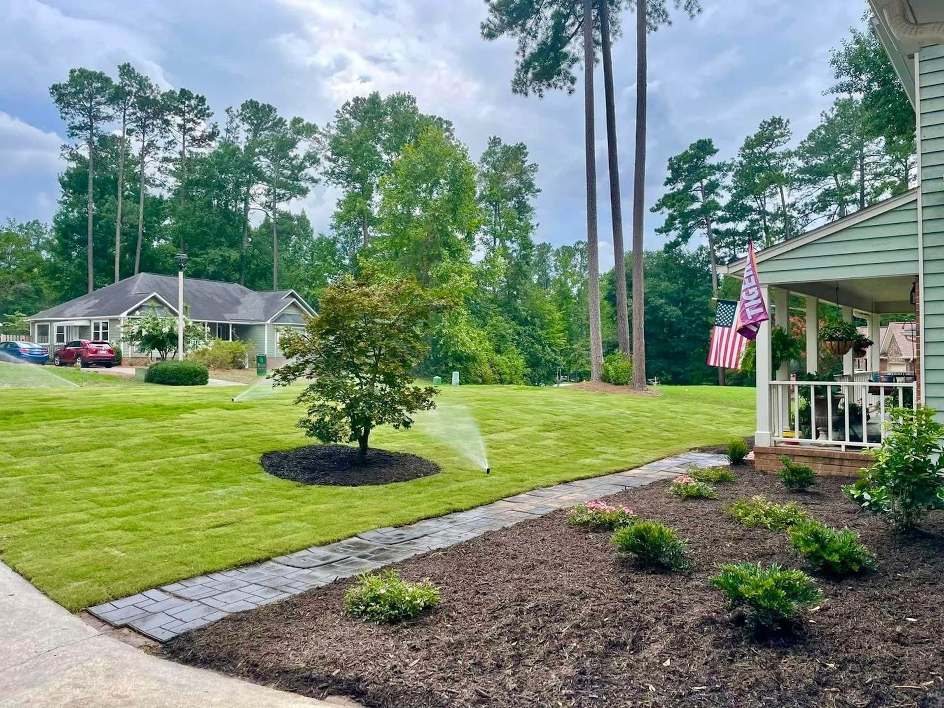 A sprinkler is spraying water on a lush green lawn in front of a house.
