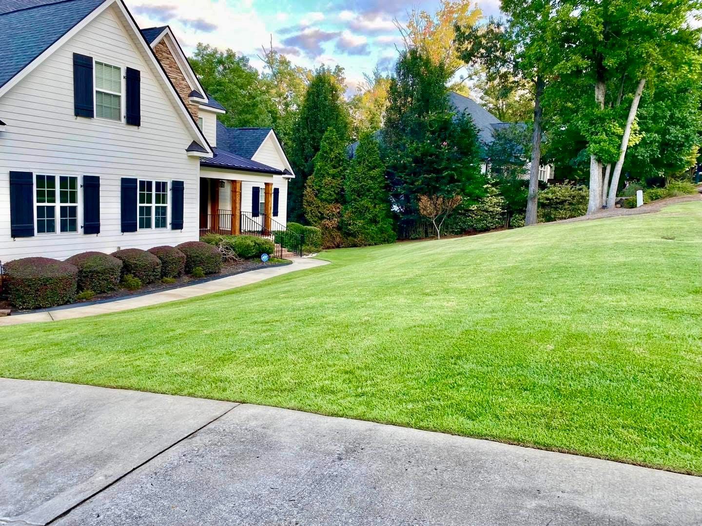 A house with black shutters and a well-manicured lawn under a partly cloudy sky.