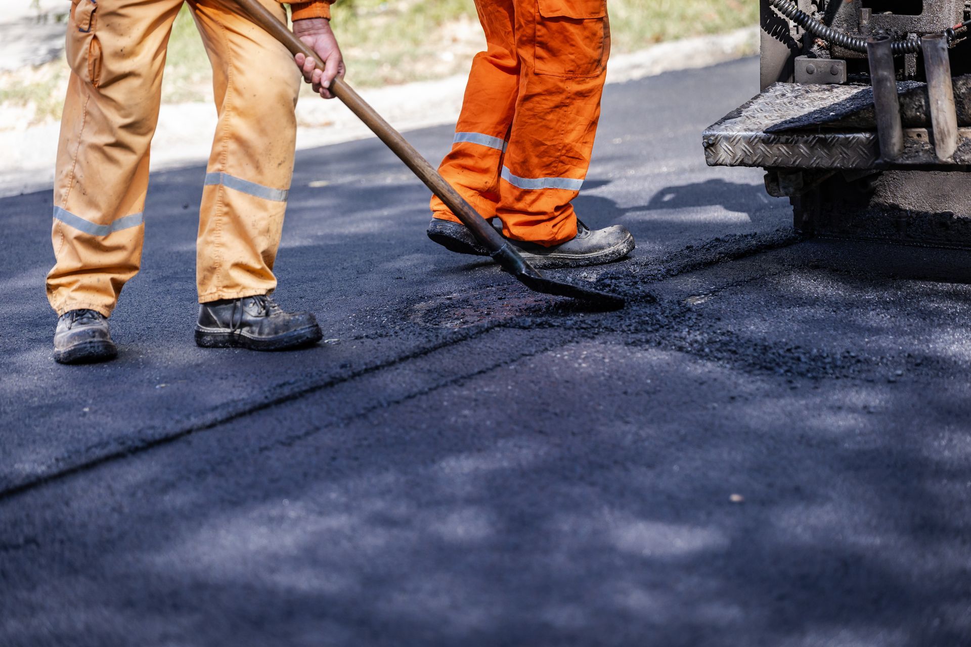 Two workers in orange pants spread asphalt with shovels on a road. Two workers in orange pants spread asphalt with shovels on a road.