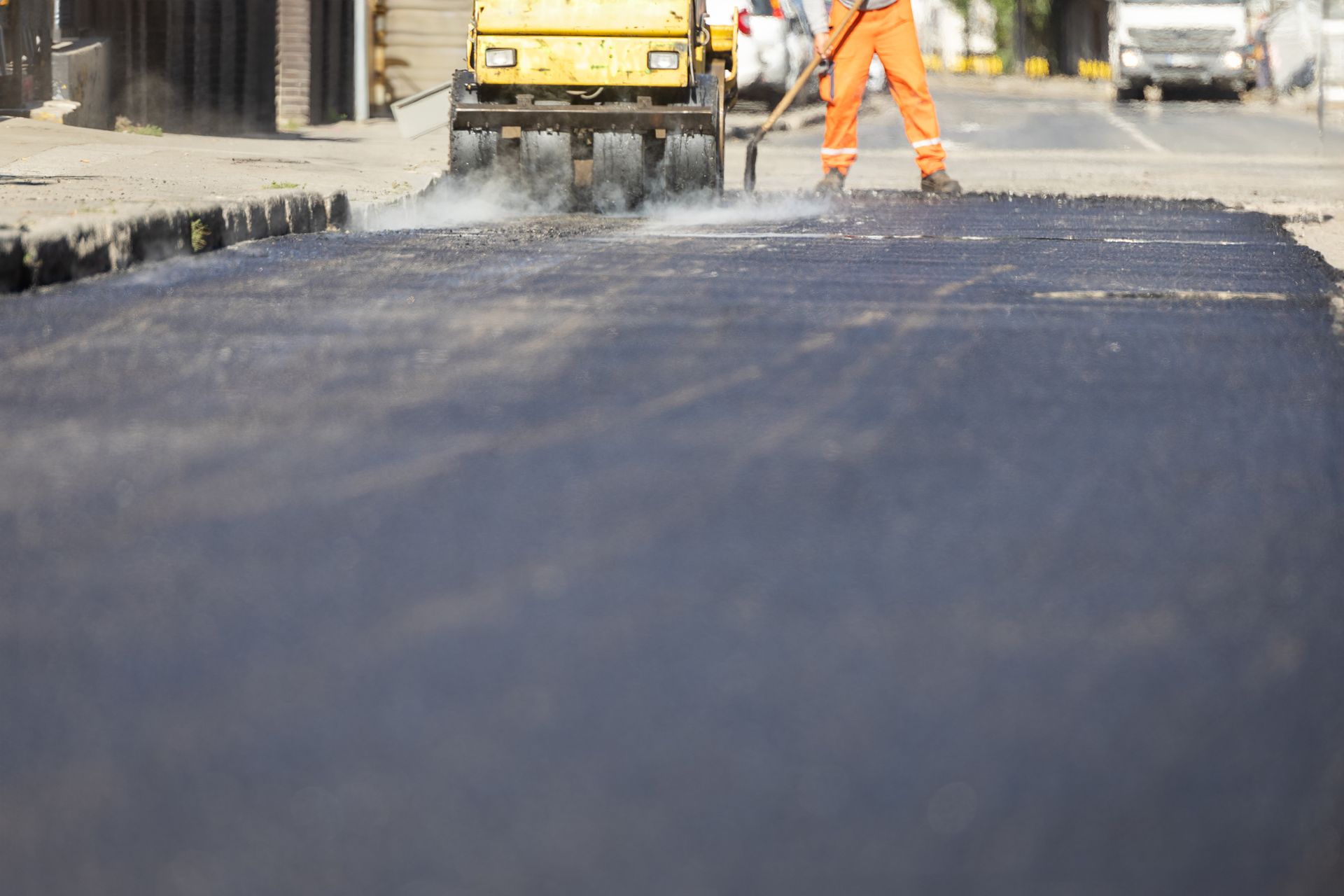 Road repair in progress; asphalt roller and worker with rake on a street, yellow and orange colors. Road repair in progress; asphalt roller and worker with rake on a street, yellow and orange colors.