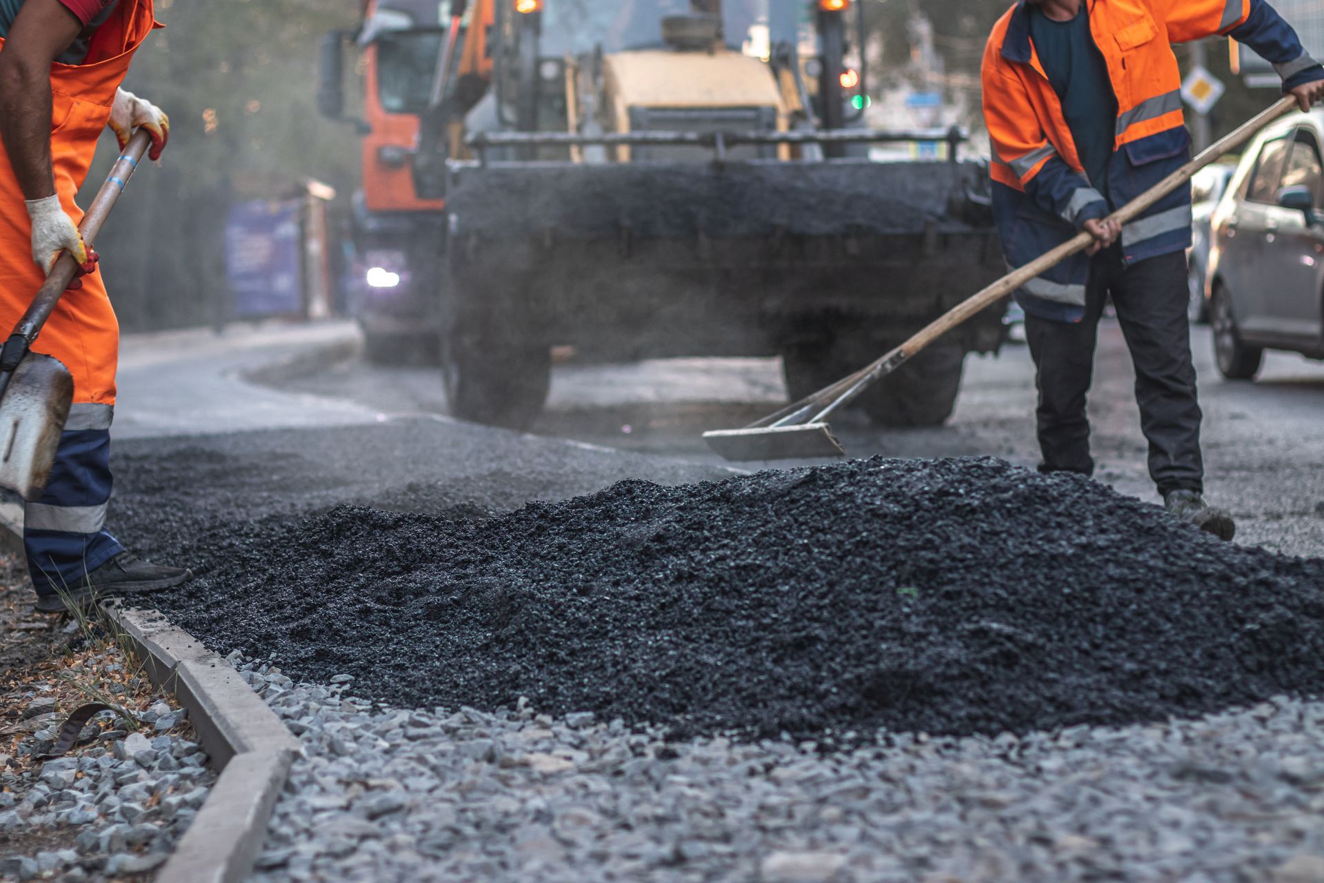 Road workers in orange vests spreading asphalt on a road, with equipment in background. Road workers in orange vests spreading asphalt on a road, with equipment in background.